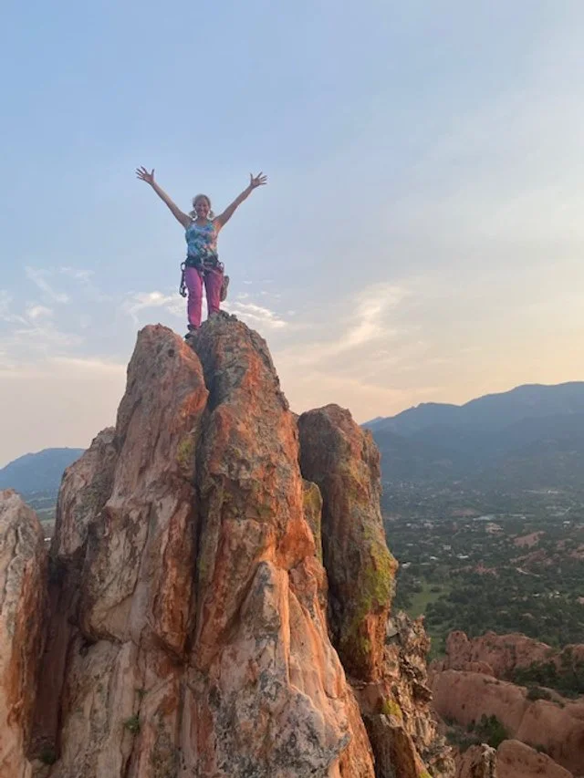 Shani standing on a mountain summit with arms raised